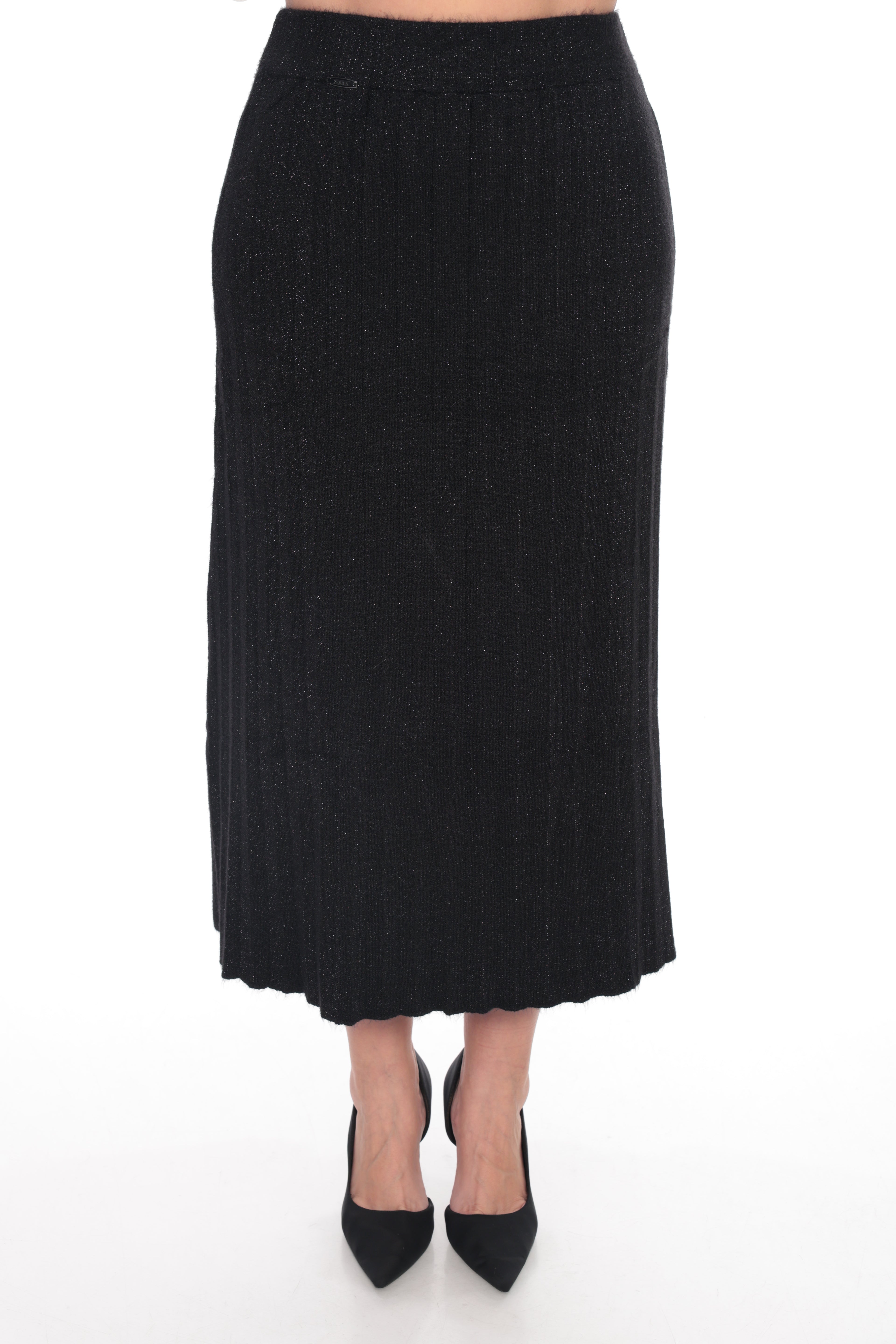 A black ribbed knit midi skirt shown on a model from the waist down, paired with black pointed-toe heels, against a plain white studio background.