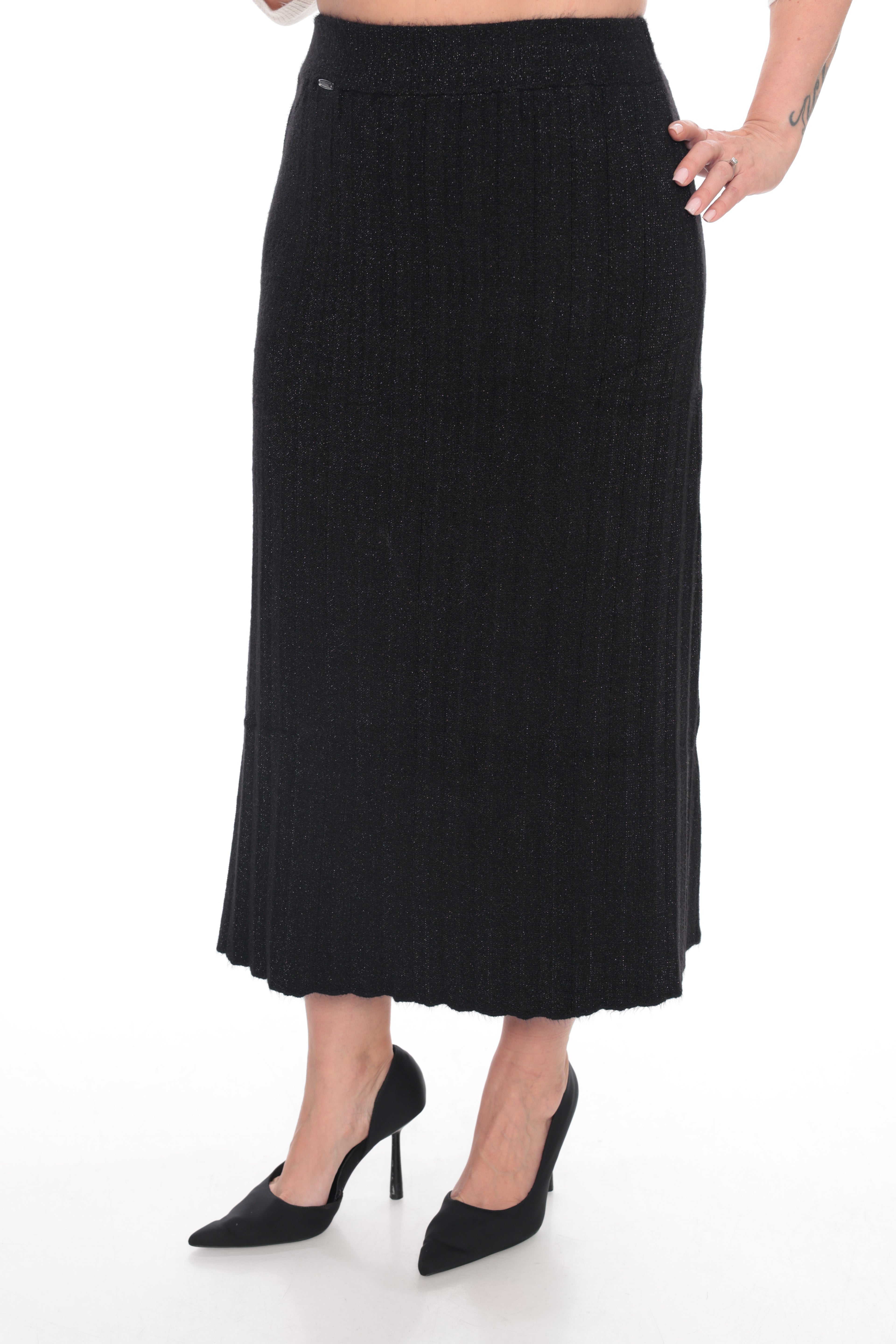 A black ribbed knit midi skirt worn by a model, paired with black pointed-toe heels, shown against a plain white studio background.
