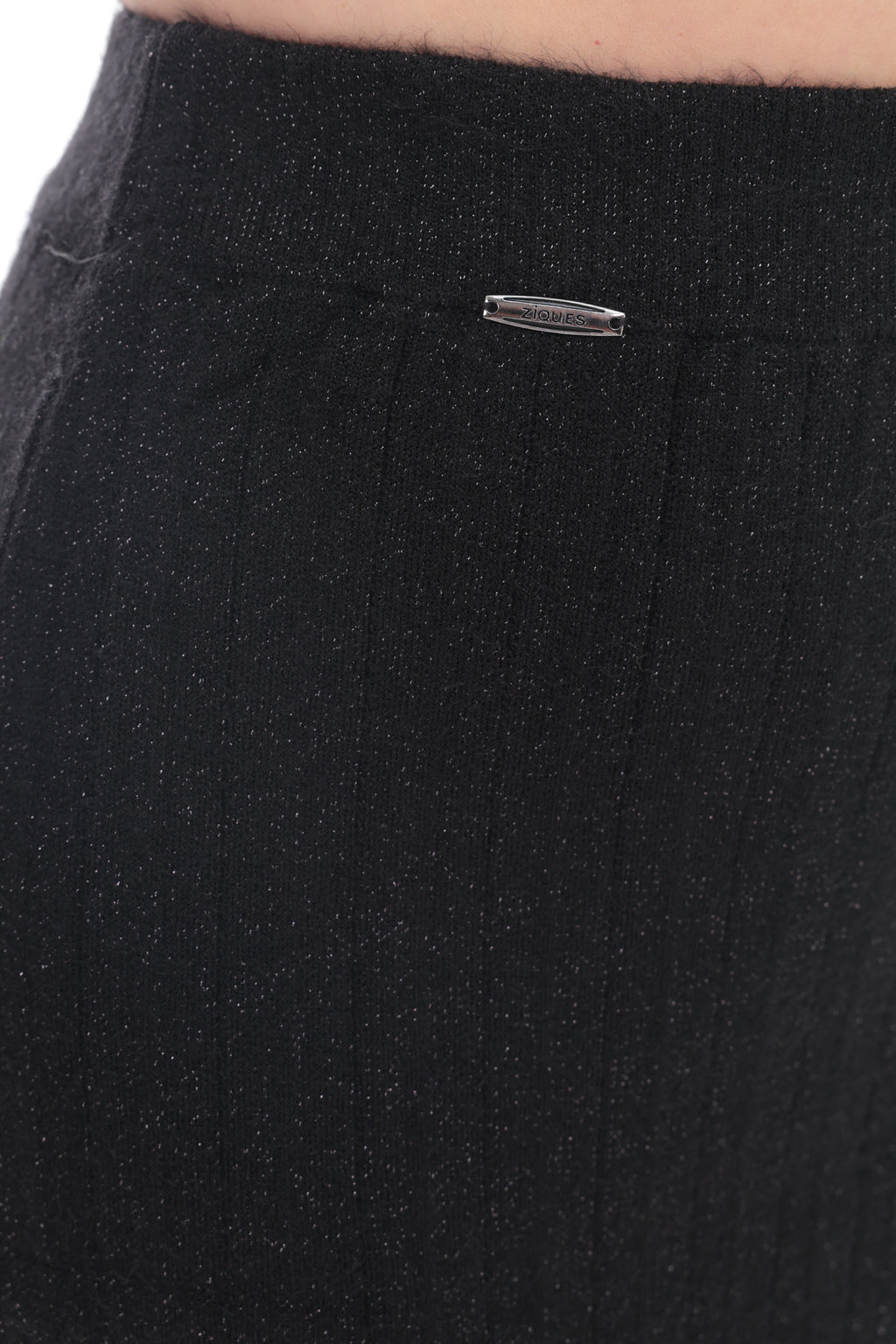 Close-up of a black ribbed knit garment, likely a skirt or shorts, showing a small silver metal brand tag near the waistband.