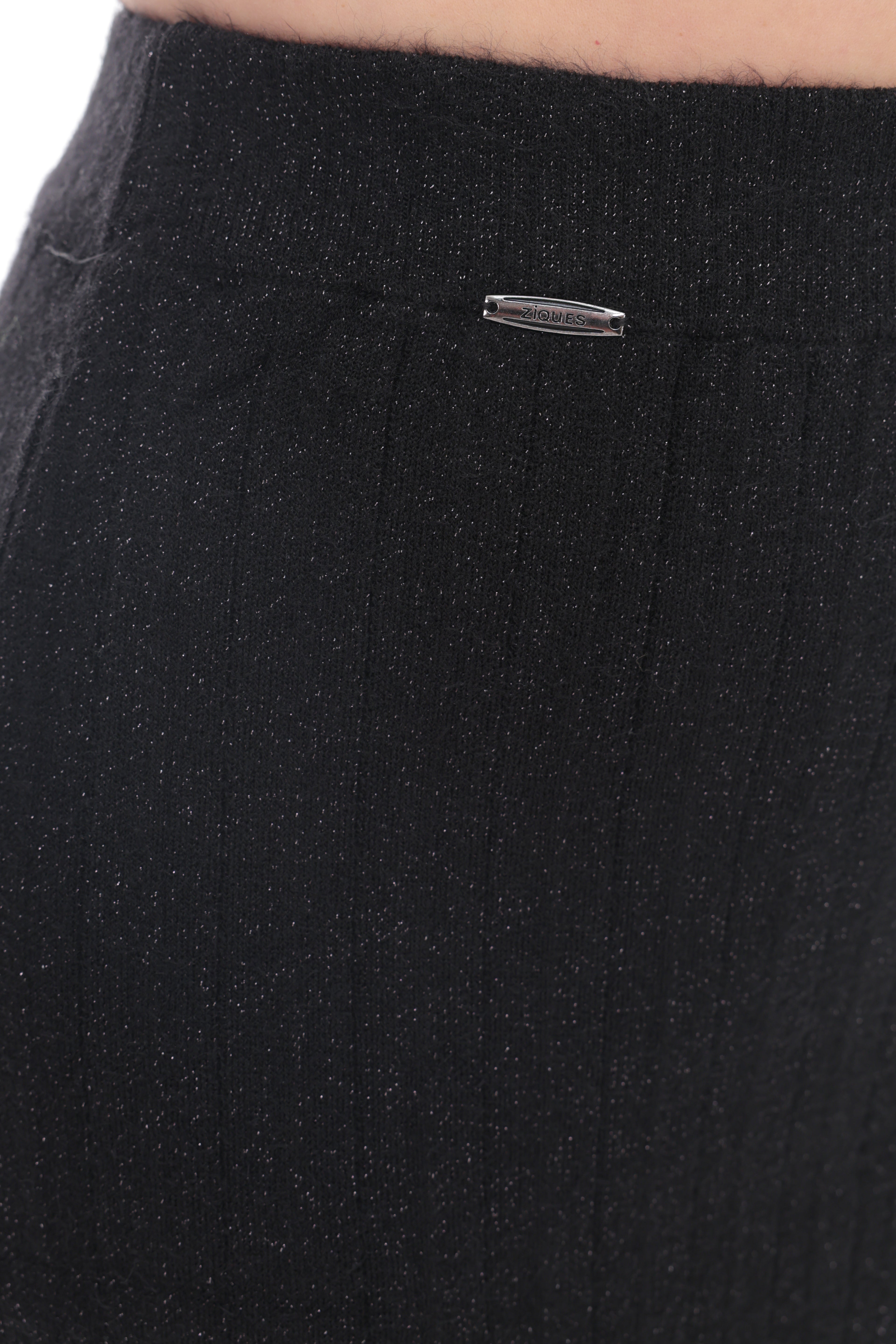 Close-up of a black ribbed knit garment, likely a skirt or shorts, showing a small silver metal brand tag near the waistband.